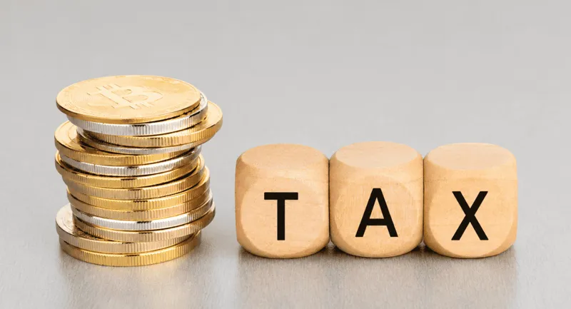 A stack of gold and silver coins beside wooden blocks spelling the word TAX