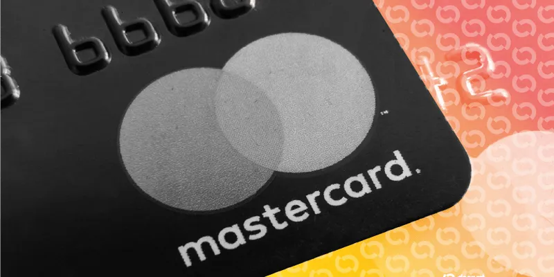 Close-up of a black Mastercard card against an orange and pink patterned background