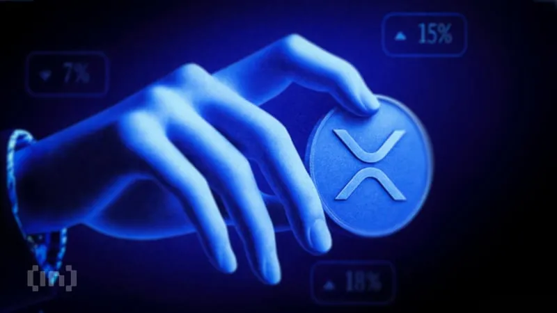 A hand holding an XRP coin against a blue background